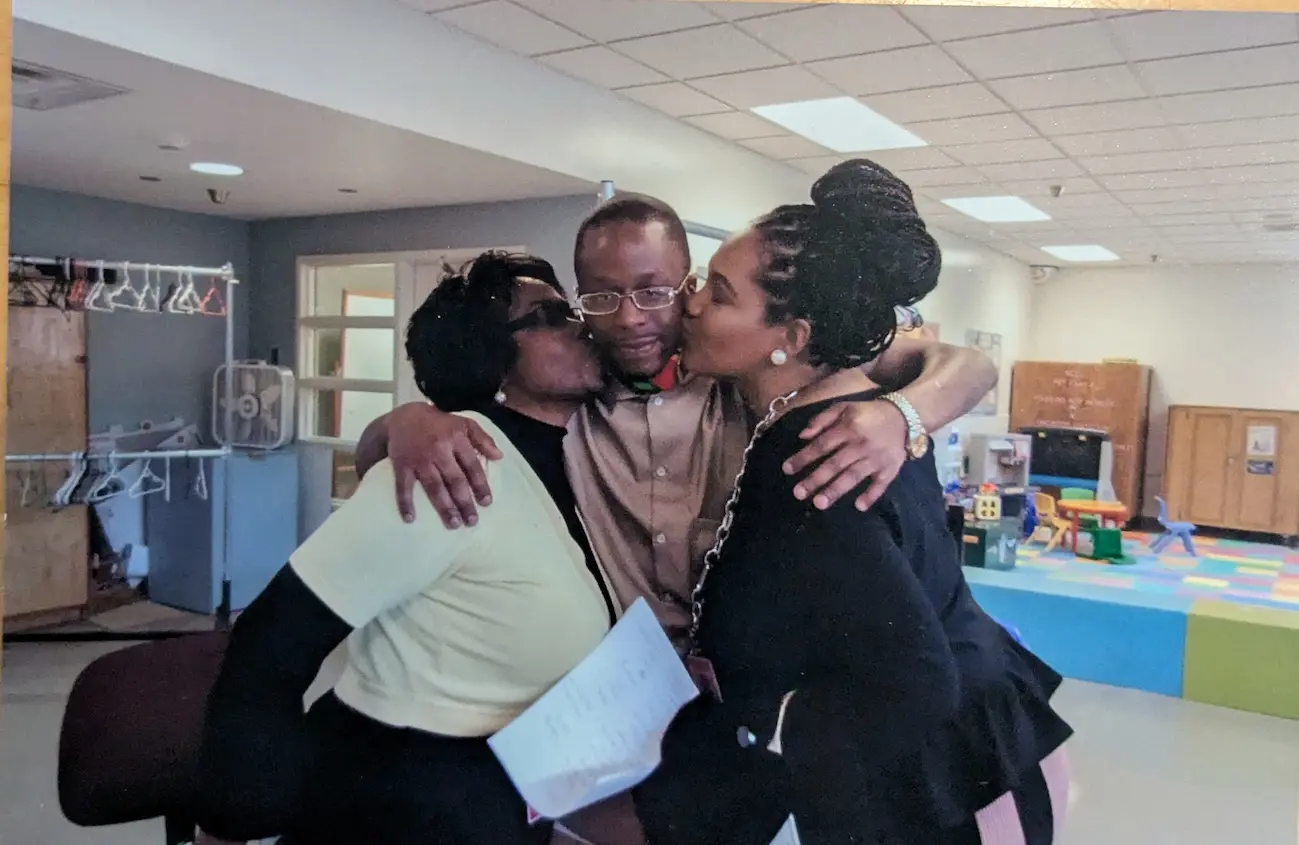L getting cheek kisses by two women in his family. His arms are around their shoulders.